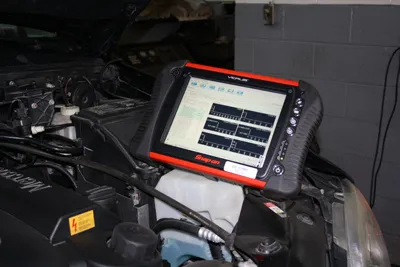 Appareil de diagnostic électronique posé sur le compartiment moteur, affichant des courbes de mesure.